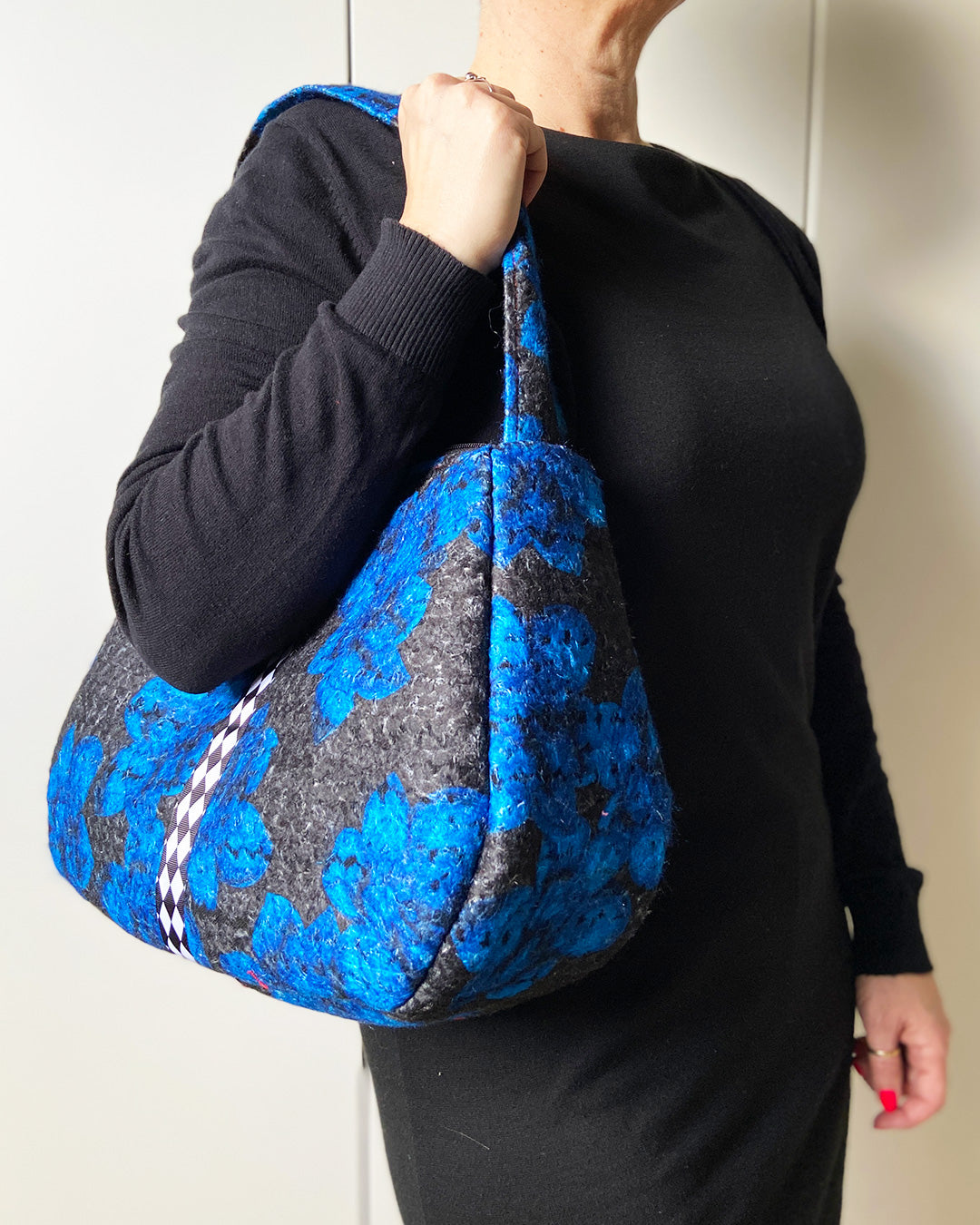 unieke, handgemaakte en stijlvolle wollen schoudertas van PIEKS creations in zwart met grote donkerblauwe bloemen en een stoere band met een grafisch zwart wit ruit - met model