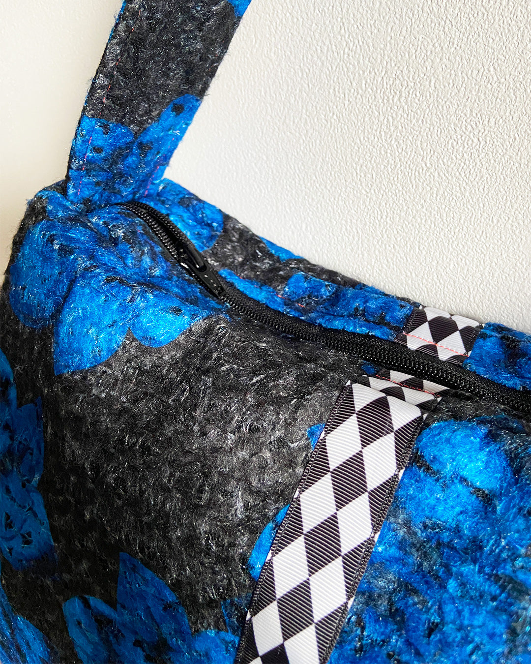 unieke, handgemaakte en stijlvolle wollen schoudertas van PIEKS creations in zwart met grote donkerblauwe bloemen en een stoere band met een grafisch zwart wit ruit  - detail met rits