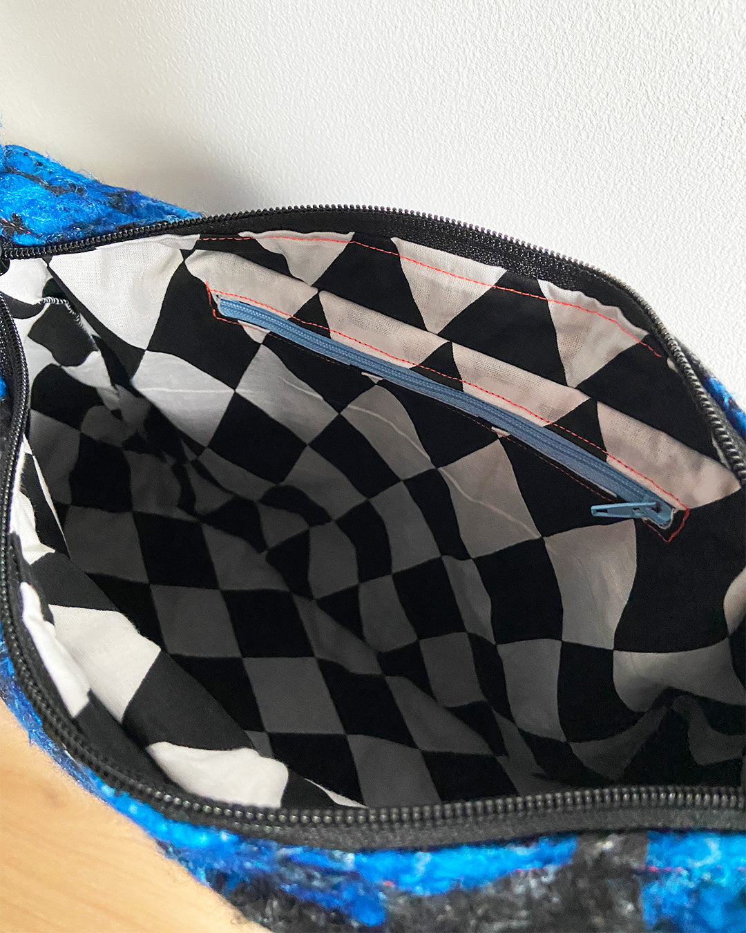 unieke, handgemaakte en stijlvolle wollen schoudertas van PIEKS creations in zwart met grote donkerblauwe bloemen en een stoere band met een grafisch zwart wit ruit  - binnenkant met zwart wit geruite voering