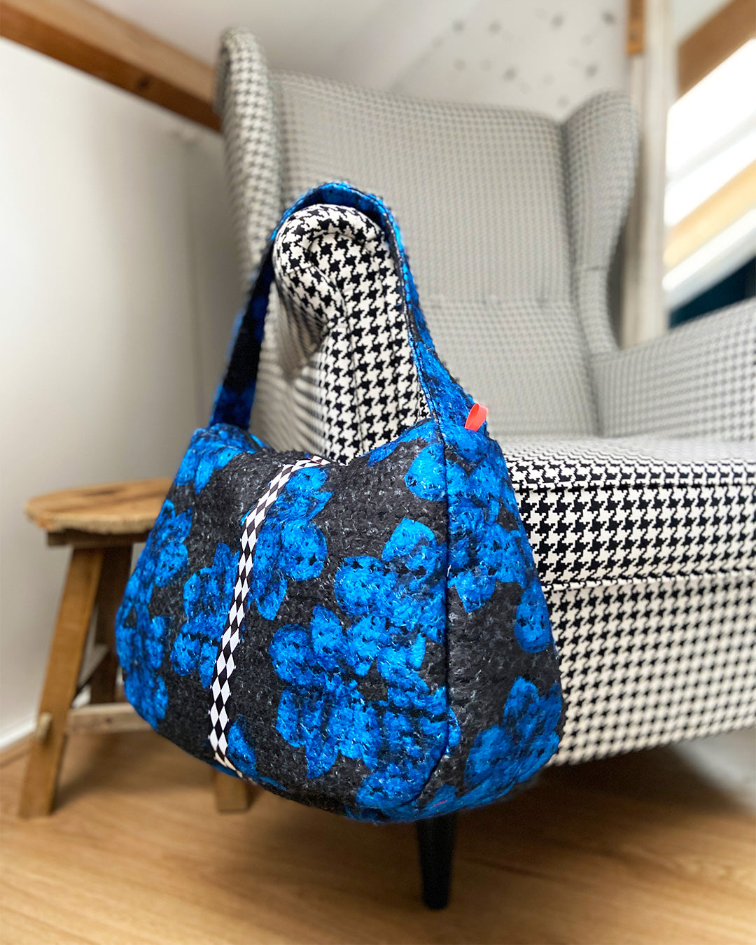 unieke, handgemaakte en stijlvolle wollen schoudertas van PIEKS creations in zwart met grote donkerblauwe bloemen en een stoere band met een grafisch zwart wit ruit  - sfeerfoto