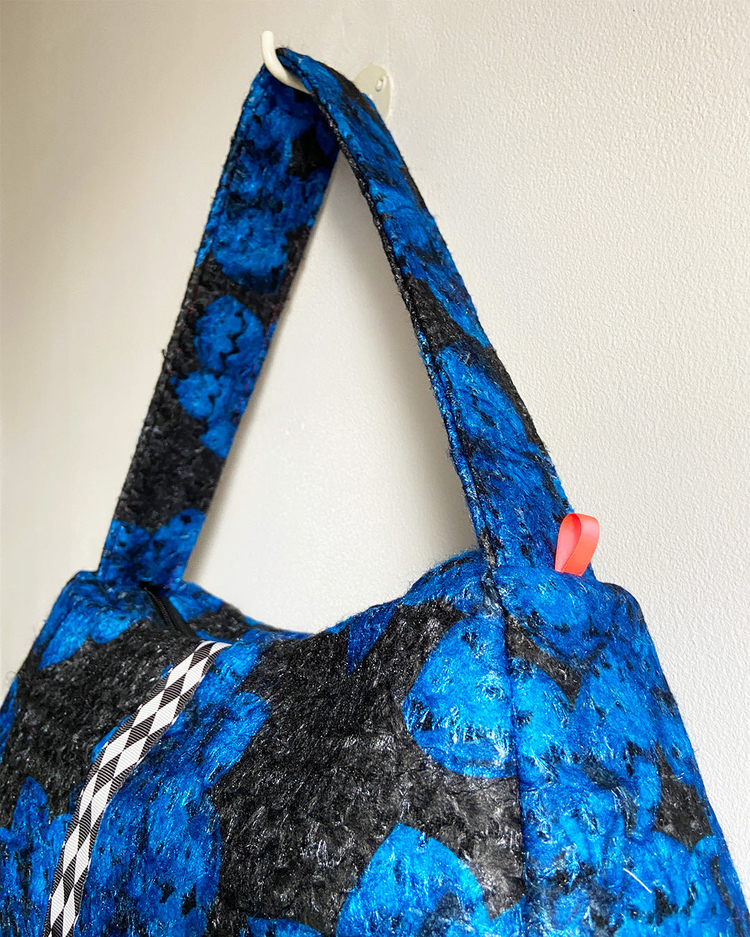 unieke, handgemaakte en stijlvolle wollen schoudertas van PIEKS creations in zwart met grote donkerblauwe bloemen en een stoere band met een grafisch zwart wit ruit  - zijkant