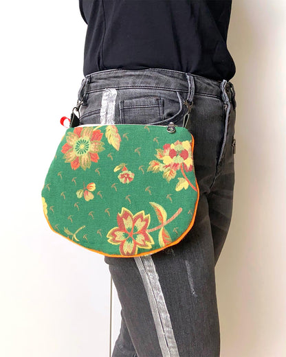 uniek, handgemaakt en kleurrijk handtasje van PIEKS creations groen met bloemen en streepjes en oranje accent - aan de broek vastgemaakt